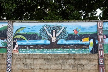 Die Wandmalerei an der Außenmauer des Internado Santa Cruz in Puerto Maldonado zeigt den Schöpfungsmythos des indigenen Volks der Harakbut. Wichtiges Symbol ist der Baum Wanamey.